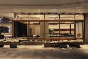 Modern indoor garden lobby at night featuring wooden structural frames, concrete pillars, stone benches, and rows of white flowering plants under warm ambient lighting.