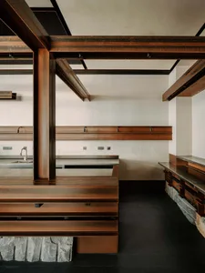 Modern kitchen interior featuring a raised platform made of weathered corten steel, massive exposed dark steel beams, minimalist white walls, and a stone base.