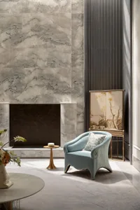 Elegant contemporary living room featuring a large marble fireplace, a curved light-blue velvet armchair with patterned cushion, a golden side table, and a traditional Chinese painted folding screen against a dark fluted wall panel.