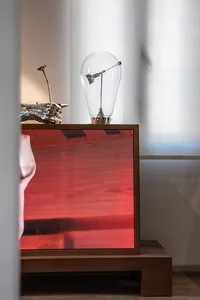 Modern walnut nightstand featuring a red mesh speaker front, a large glass teardrop lamp, and a silver metallic hand sculpture holding a dried flower.