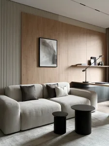 Modern minimalist living room featuring a light beige modular sofa with grey and beige cushions, two black cylindrical side tables, light oak wood wall paneling with vertical slats, and a black-framed abstract artwork.