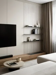 Modern minimalist living room featuring a wall-mounted TV, light oak media console, floating glass shelves with decor, and neutral-toned sofa with round coffee table.