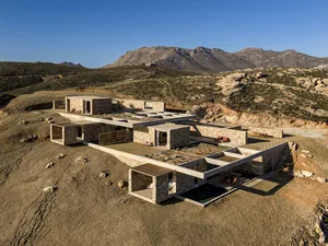 Aerial view of a modern stone and concrete courtyard villa built into a dry mountainous landscape under a clear blue sky.