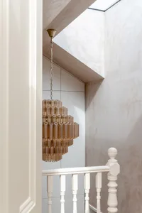 View of a modern white staircase with turned balusters, featuring a large amber acrylic tiered chandelier hanging from a skylight.