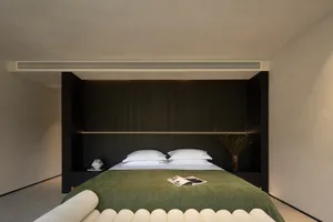 Modern minimalist bedroom with dark wood built-in headboard, white bedding, olive green textured throw blanket, and integrated LED lighting.