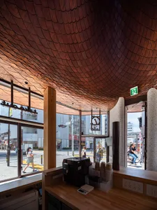 Interior view of a modern Tokyo cafe featuring a dramatic scalloped wooden ceiling, wooden service counter with coffee equipment, and large street-facing windows.