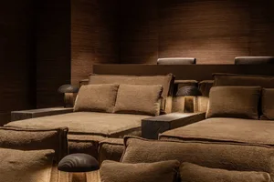 Low-profile modular sofa upholstered in rich brown boucle fabric, arranged with multiple textured cushions, set against dark wood panel walls and illuminated by three black mushroom table lamps.