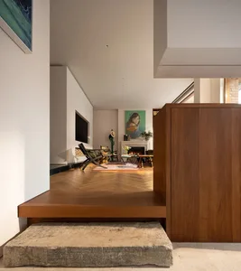 View from a stone step looking into a modern split-level living room featuring herringbone wood floors, a walnut partition wall, fireplace, and colorful artwork.