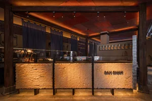 Modern Japanese-inspired cafe interior featuring a massive textured stone counter with backlit 'SAN SHAN' signage, dark timber structural beams, and warm ambient lighting.