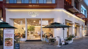 Modern white cafe exterior at night with green outdoor seating, large glass windows, and warm interior lighting showing patrons inside.