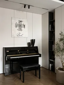 Black Yamaha upright piano with leather bench, Bach music artwork on the wall, built-in shelving, and potted olive tree in a minimalist interior