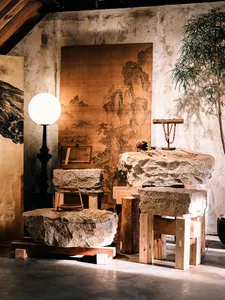 侘寂風藝術工作室內部，展示大型原石塊作為桌椅使用、木製支架、大型中國山水畫、球形立燈與盆栽樹木。