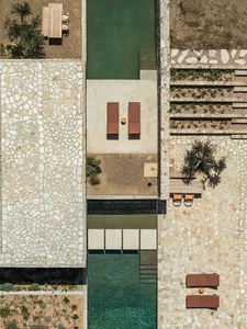 Aerial photograph of a luxury villa featuring a long rectangular infinity pool, stone-paved terraces, terracotta lounge chairs, and a dining area surrounded by arid landscaping.