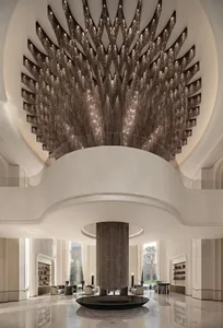 Luxurious modern hotel lobby featuring an enormous sculptural crystal chandelier hanging from a circular ceiling opening, with polished marble floors and minimalist white architectural details.