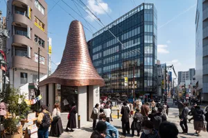 Daytime view of a distinctive copper conical roof building surrounded by pedestrians on a busy street in Kichijoji, Tokyo, with modern glass buildings in the background.