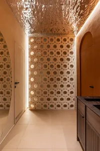 Modern minimalist hallway featuring a large terracotta perforated screen wall, matching curved walls, textured metallic ceiling, and warm ambient lighting.