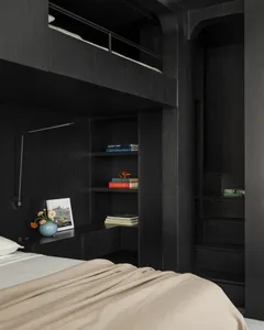 Modern dark wood loft bedroom featuring a raised sleeping platform, built-in bookshelves, a wall-mounted reading lamp, and neutral bedding with soft beige tones.