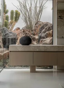 Modern minimalist bathroom featuring a floating travertine vanity with a black ceramic vessel, large glass window overlooking dramatic desert rocks and cacti.