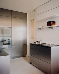Modern minimalist kitchen featuring seamless stainless steel cabinetry, built-in appliances, dark stone countertop, and white floating shelves with wooden storage boxes.