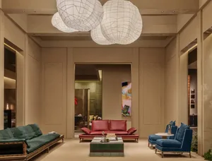 Modern luxury hotel lobby featuring a red leather sofa, teal velvet daybed, blue velvet armchairs, and large white paper lanterns hanging from the ceiling.