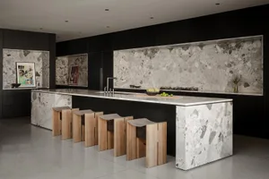 Modern kitchen with large white and grey terrazzo island and matching backsplash, black cabinetry, and six sculptural light-wood bar stools lined up in front.
