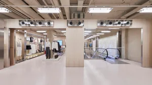 Wide view of a modern minimalist clothing boutique interior with concrete pillars, light birch wood partitions, white floors, and exposed ceiling infrastructure.