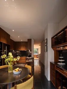 Modern kitchen and dining area featuring walnut wood cabinetry, black stone floor tiles, round dark dining table, and mustard yellow upholstered chairs.