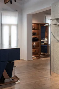 Modern minimalist entryway featuring a blue upholstered bench with walnut base, built-in walnut display shelves with decorative objects, light wood flooring, and a textured beige wall panel.