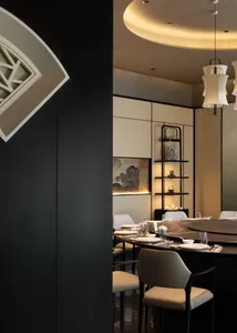 Elegant Chinese restaurant interior with a large round dark dining table, cream upholstered chairs, silk lanterns, and traditional Chinese artwork on a textured wall.