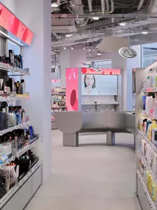 Modern cosmetics store interior with curved grey central island, pink digital display walls, and neatly organized product shelves under bright track lighting.