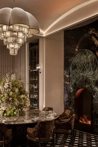 Luxurious dining room featuring a large round marble table, velvet patterned dining chairs, a striking green marble fireplace with arched opening, and an oversized cloud-like chandelier with multiple lit tiers.