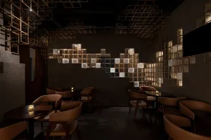 Dimly lit modern restaurant interior featuring brown leather dining chairs, dark round tables, and a striking illuminated brass cube grid art installation covering the back wall.