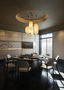 Modern Chinese-style dining room with a large round black marble table, eight cream upholstered chairs, textured wall panels, ink wash painting, and a sculptural cluster of cylindrical pendant lights hanging from a circular ceiling feature.