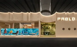 Modern Pablo showroom interior featuring an undulating textured plaster wall with integrated lighting, displaying colorful lounge chairs against a vibrant blue wave mural and a moss wall installation.