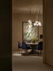 Elegant modern dining room with round pedestal table, four blue velvet dining chairs, large abstract painting, and multiple spherical pendant lights hanging from the ceiling.