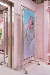 Freestanding stainless steel digital screen displaying a portrait of a woman, set against glossy pink tiled walls in a modern retail space