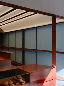 Modern bakery interior featuring warm walnut wood counters, glass pastry display case filled with croissants, and linear LED lighting integrated into the ceiling.