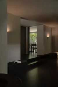 Modern minimalist interior featuring a dark concrete reading nook with built-in black leather bench, open book, and view to a lush green garden through a large opening.
