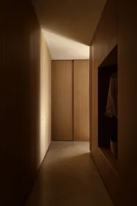 Narrow walk-in closet hallway featuring full-height oak wood cabinetry, built-in drawers, open hanging space, and dramatic ceiling cove lighting on a polished concrete floor.