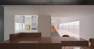 Modern minimalist dining area featuring a large terracotta tiled counter with integrated banquette seating, wooden chairs, white walls, and a view into a long corridor with wooden flooring.