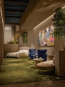 Modern bedroom lounge featuring two deep blue velvet armchairs, a round boucle chaise, colorful abstract painting, and lush greenery under warm ambient lighting.
