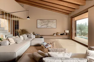 Modern organic living room featuring a large L-shaped neutral sofa, tree-trunk coffee table, exposed wooden ceiling beams, and large sliding glass doors opening to a garden.