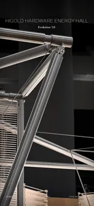 Close-up view of polished stainless steel pipes and mechanical joints forming an architectural structure with tension cables and blinds in the background.