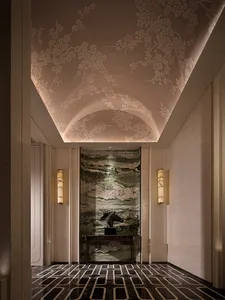 Luxurious hallway with vaulted ceiling carved with plum blossom pattern, green marble feature wall, dark horse head sculpture on console table, and geometric black marble floor.
