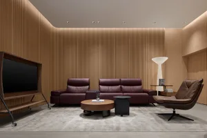 Modern minimalist living room featuring a burgundy leather sofa, matching loveseat, brown leather swivel chair, round wooden coffee table, vertical wood slat walls, and a white floor lamp on a light grey rug.