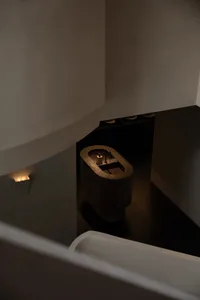 High-angle view of a minimalist dark bathroom featuring a freestanding concrete bathtub, recessed wall lighting, and dark flooring.