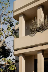 Close-up view of a modern building with curved concrete balconies, structural pillars, and potted plants under a clear blue sky.