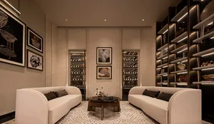 Modern luxury living room with two curved cream sofas, dark marble coffee table, patterned rug, and illuminated wine cellar display cases built into the back wall.