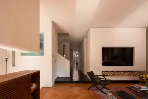 Modern minimalist living room featuring herringbone oak flooring, a recessed fireplace with stacked firewood, a black wooden lounge chair on a Persian rug, and clean white architectural walls.