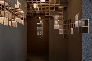 Narrow corridor of a modern wine cellar featuring dark textured plaster walls and an intricate system of illuminated copper and glass grid shelves displaying wine bottles.